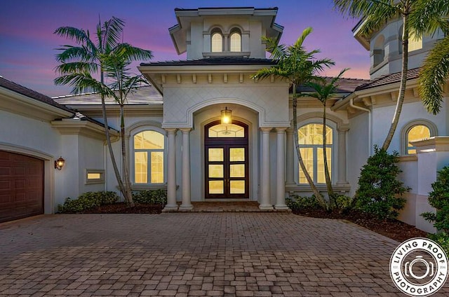 exterior entry at dusk with decorative driveway and stucco siding