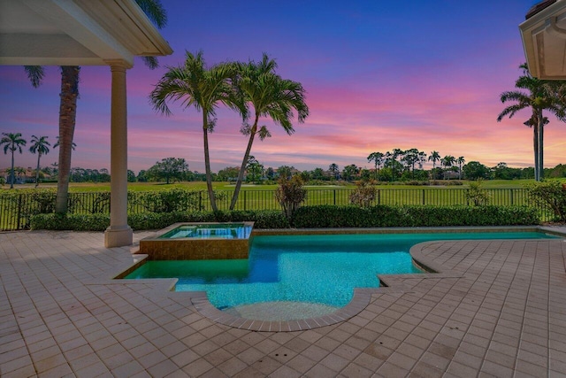 pool at dusk with a fenced backyard, a pool with connected hot tub, and a patio area