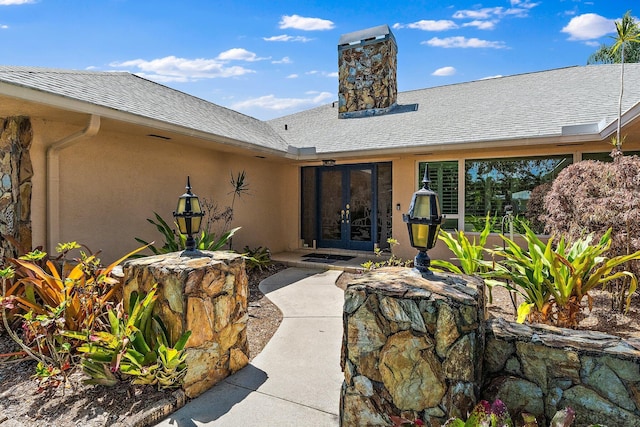 1256 Holly Cove Dr, Jupiter, FL 33458 - view of exterior entry featuring a chimney, french doors, a shingled roof, and stucco siding