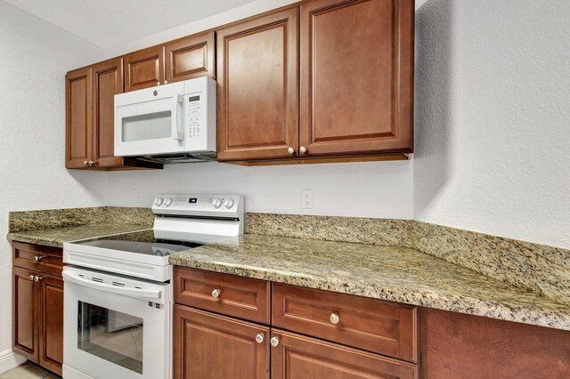 kitchen featuring brown cabinetry, white appliances, and light stone countertops