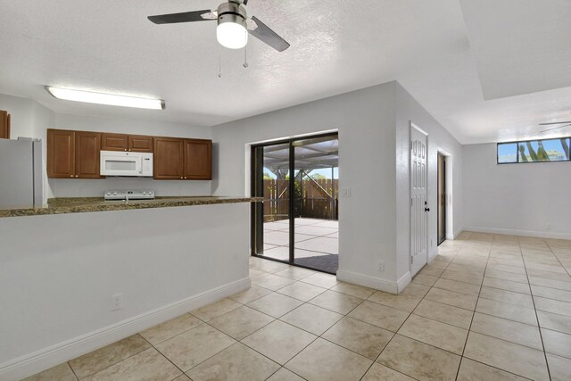 kitchen featuring white appliances, baseboards, ceiling fan, brown cabinets, and light tile patterned floors