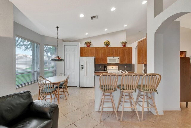 12249 Blair Ave, Boynton Beach, FL 33437 - kitchen featuring brown cabinetry, visible vents, arched walkways, lofted ceiling, and white appliances