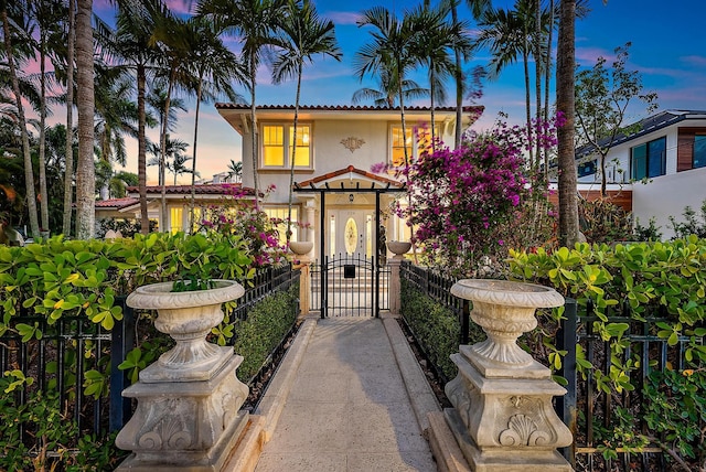 mediterranean / spanish house featuring stucco siding, a fenced front yard, a tile roof, and a gate