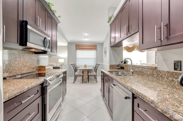 kitchen with appliances with stainless steel finishes, a sink, baseboards, light tile patterned floors, and tasteful backsplash