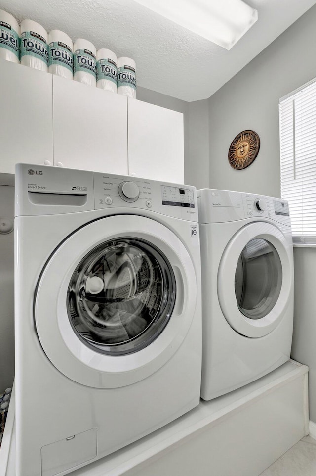 laundry area with washer and clothes dryer, cabinet space, and a textured ceiling