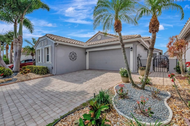 mediterranean / spanish home featuring a garage, a gate, stucco siding, and decorative driveway