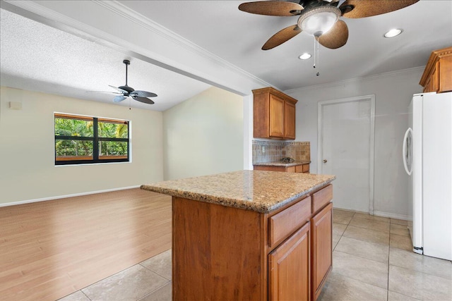 12610 63rd Ln N, The Acreage, FL 33412 - kitchen featuring ceiling fan, brown cabinetry, freestanding refrigerator, backsplash, and a kitchen island