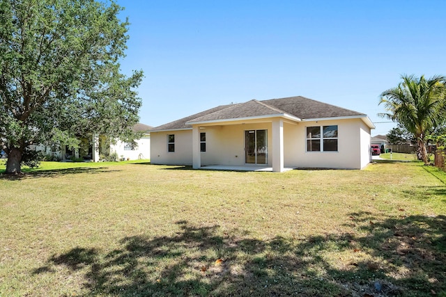565 SW Feldman Ave N, Port Saint Lucie, FL 34953 - back of property featuring a lawn, a patio, stucco siding, and roof with shingles