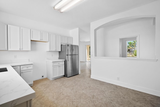 565 SW Feldman Ave N, Port Saint Lucie, FL 34953 - kitchen with freestanding refrigerator, light stone countertops, baseboards, white cabinets, and arched walkways