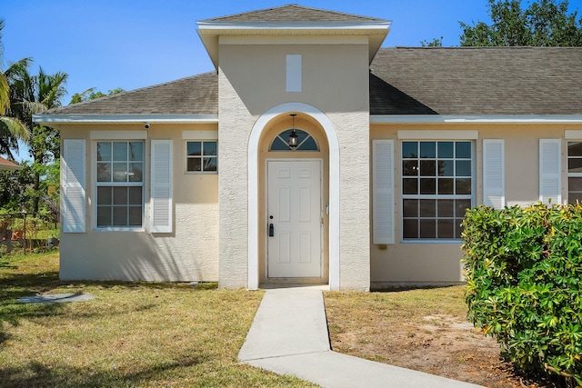 565 SW Feldman Ave N, Port Saint Lucie, FL 34953 - view of exterior entry with roof with shingles, stucco siding, and a yard