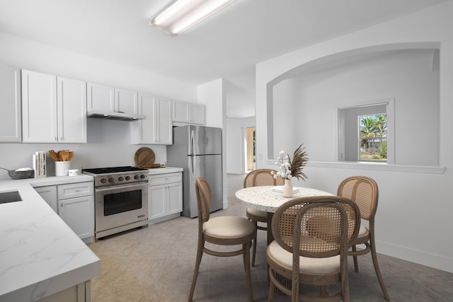 565 SW Feldman Ave N, Port Saint Lucie, FL 34953 - kitchen with arched walkways, white cabinets, stainless steel appliances, and under cabinet range hood