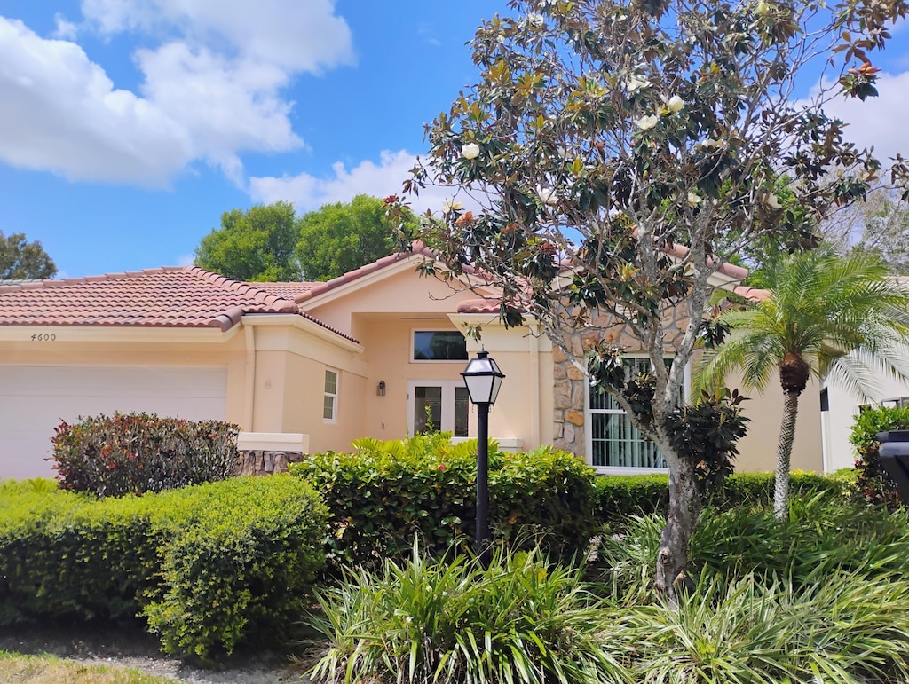 mediterranean / spanish home with a garage, stucco siding, a tiled roof, and stone siding