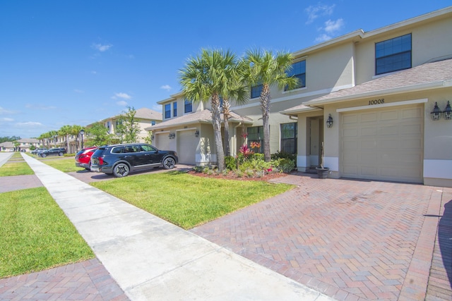 view of front of property featuring an attached garage, decorative driveway, stucco siding, and a front yard