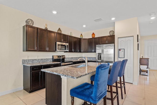 kitchen featuring visible vents, appliances with stainless steel finishes, a sink, light tile patterned floors, and light stone counters