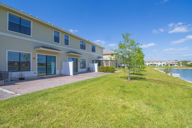 rear view of property with central AC unit, a patio, a yard, a water view, and stucco siding