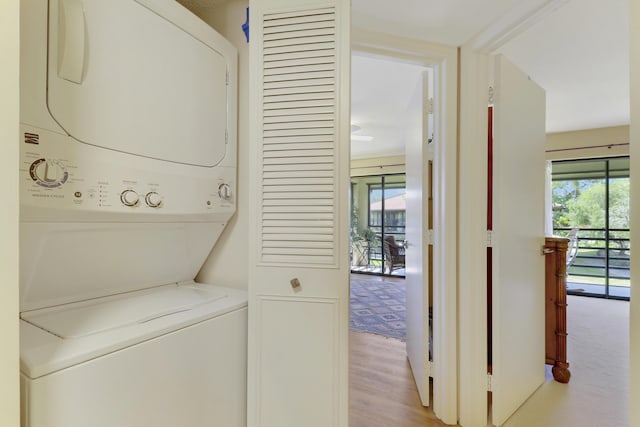 clothes washing area with laundry area, wood finished floors, stacked washer / dryer, and a wealth of natural light
