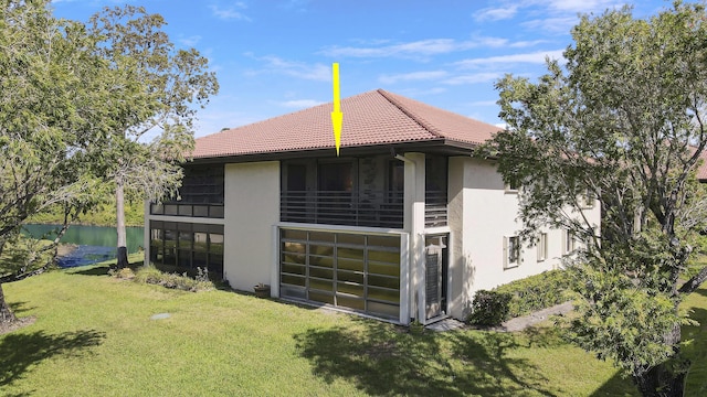 view of side of property with a lawn, a tiled roof, a water view, and stucco siding