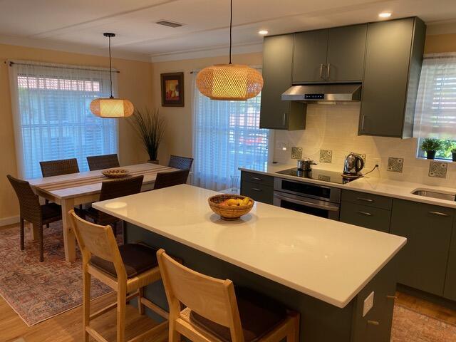671 SW S River Dr Unit 207, Stuart, FL 34997 - kitchen with under cabinet range hood, stainless steel oven, black electric stovetop, light countertops, and backsplash