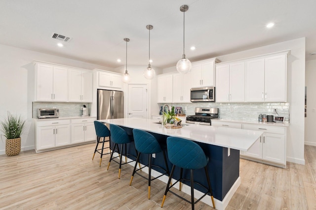 14175 SW Harker St, Port Saint Lucie, FL 34987 - kitchen featuring appliances with stainless steel finishes, decorative backsplash, light countertops, a breakfast bar area, and a center island with sink