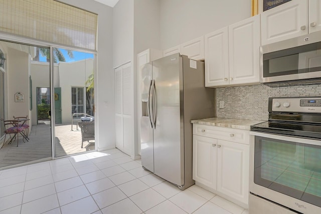 kitchen featuring white cabinets, a high ceiling, appliances with stainless steel finishes, light tile patterned floors, and backsplash