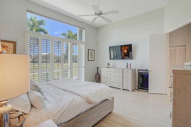 bedroom with ceiling fan, a high ceiling, and light wood-style flooring