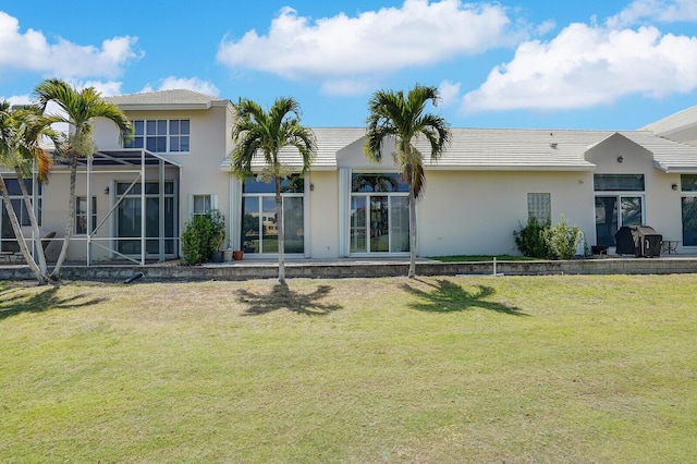 rear view of property featuring a lawn, a lanai, and stucco siding