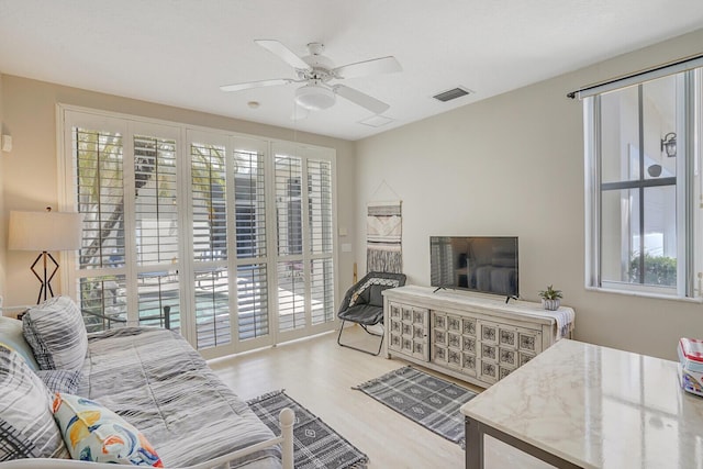 living area featuring visible vents, a ceiling fan, wood finished floors, and a wealth of natural light
