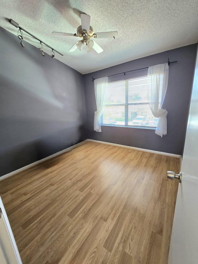 spare room featuring ceiling fan, a textured ceiling, wood finished floors, track lighting, and baseboards