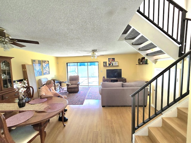 living area with light wood-style floors, a ceiling fan, a textured ceiling, and stairs