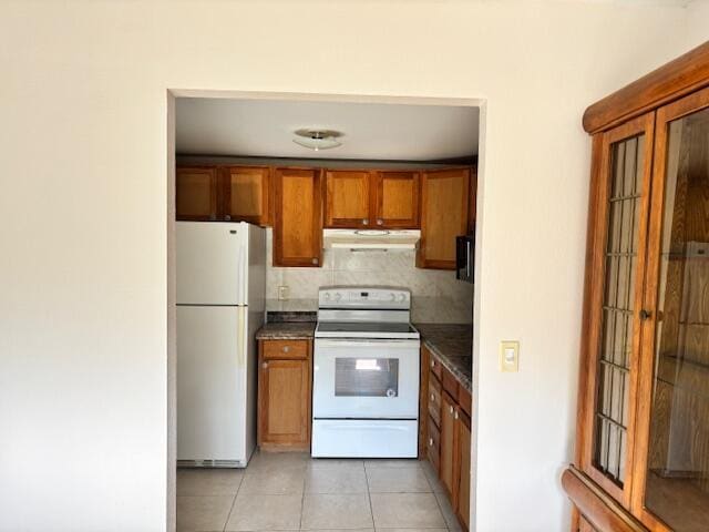 kitchen featuring brown cabinetry, light tile patterned floors, under cabinet range hood, and white appliances