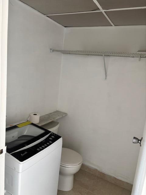 bathroom with baseboards, washer / clothes dryer, tile patterned flooring, and toilet
