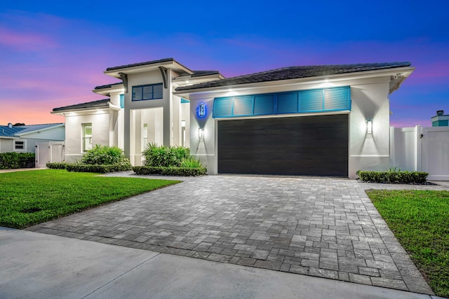 prairie-style home with a lawn, stucco siding, an attached garage, and decorative driveway