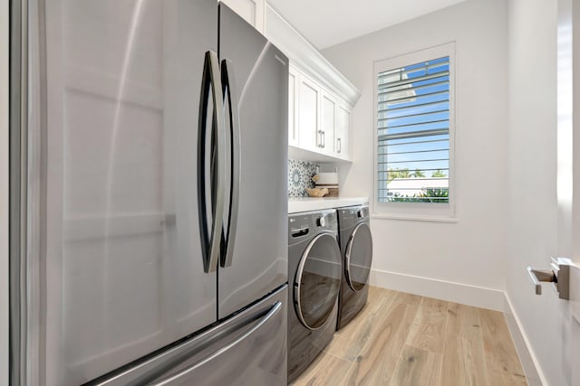 laundry area with cabinet space, baseboards, light wood-style flooring, and washing machine and clothes dryer