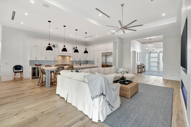 living room with recessed lighting, light wood finished floors, ceiling fan with notable chandelier, and baseboards