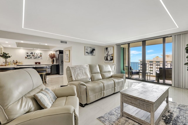 living area featuring indoor wet bar, light tile patterned floors, a tray ceiling, visible vents, and expansive windows