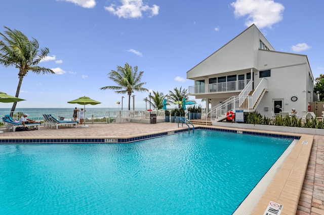 community pool with a water view, fence, stairs, and a patio area