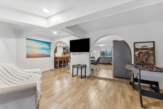 living area featuring arched walkways, beam ceiling, baseboards, recessed lighting, and light wood-style flooring
