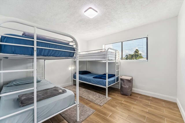 bedroom with a textured ceiling, baseboards, and wood finished floors