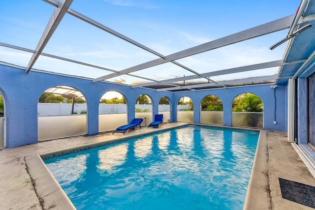 outdoor pool featuring glass enclosure, fence, and a patio area