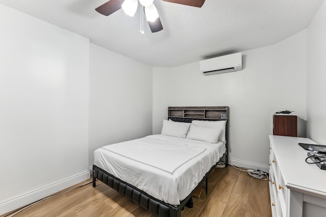 bedroom featuring a ceiling fan, a textured ceiling, a wall mounted air conditioner, wood finished floors, and baseboards