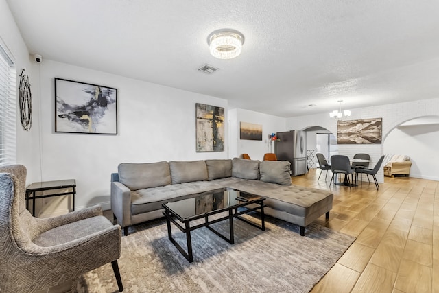 living area featuring an inviting chandelier, arched walkways, a textured ceiling, light wood-type flooring, and visible vents