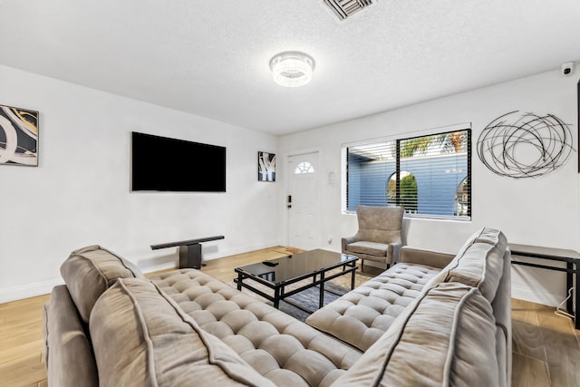 living room featuring a textured ceiling, baseboards, visible vents, and wood finished floors