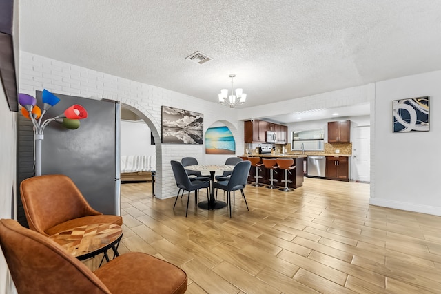 dining area with visible vents, an inviting chandelier, a textured ceiling, arched walkways, and light wood-style flooring
