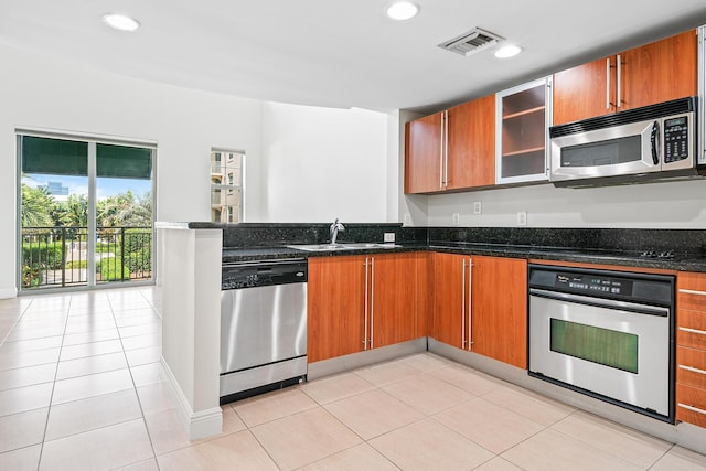 kitchen with visible vents, a peninsula, a sink, dark stone countertops, and stainless steel appliances