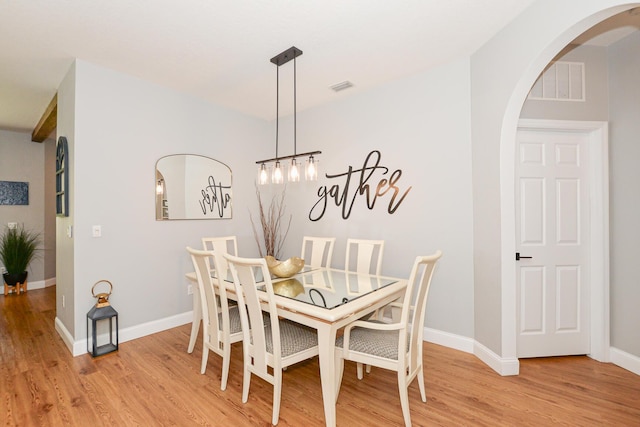 dining space with arched walkways, baseboards, light wood-style flooring, and visible vents
