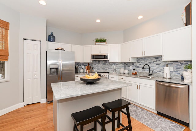 kitchen with light wood-style floors, white cabinets, tasteful backsplash, a sink, and appliances with stainless steel finishes