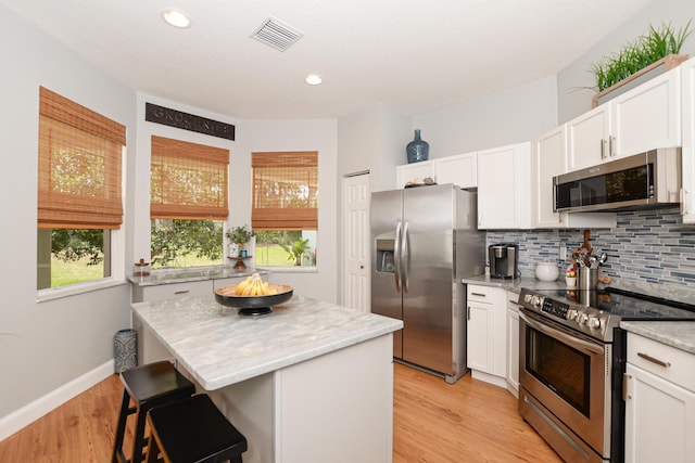 kitchen featuring appliances with stainless steel finishes, white cabinets, backsplash, and visible vents