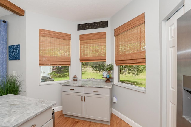 interior space featuring baseboards, light wood finished floors, and beamed ceiling