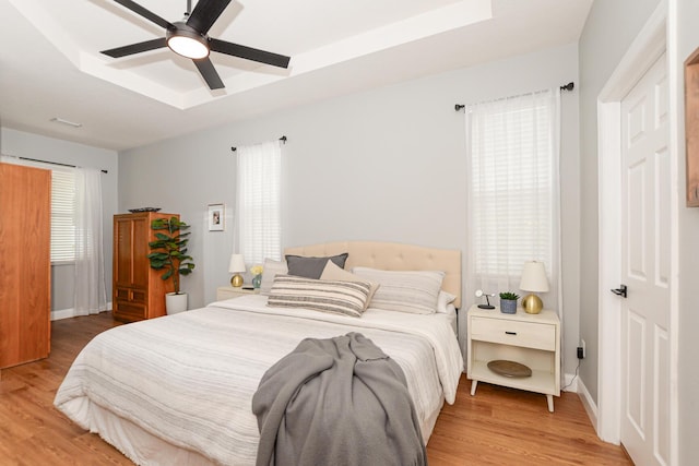 bedroom featuring a raised ceiling, multiple windows, and light wood finished floors