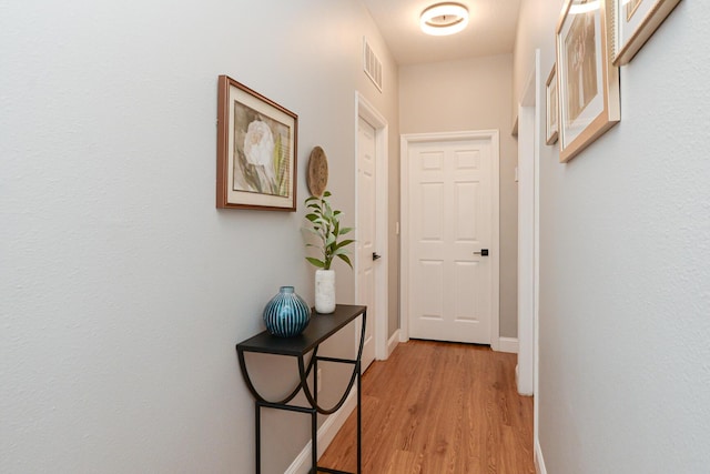 hall with baseboards, visible vents, and light wood-style floors
